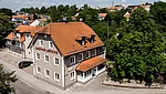 Sicht auf das Gasthofgebäude von oben, Vorderansicht zur Straße mit Biergarten und Baumbestand