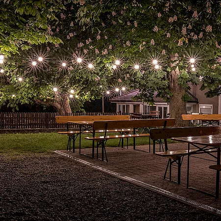 Bierzeltgarnituren im Biergarten, nachts, mit Beleuchtung Lichterkette
