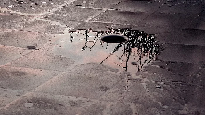 Pflasterboden mit kleiner Regenpfütze und Abflussloch