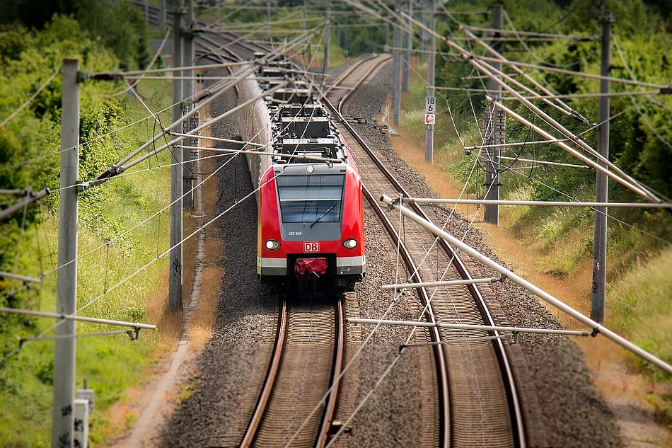 Roter DB-Zug fährt auf elektrischen Gleisen durch grüne Landschaft mit Bäumen entlang der Strecke.