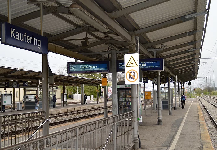 Bahnsteig mit Überdachung, Fahrgastinformationsanzeigen und Schild mit dem Stationsnamen Kaufering